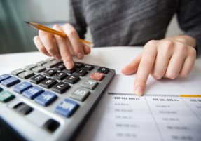 Closeup of accountant counting on calculator and working with table